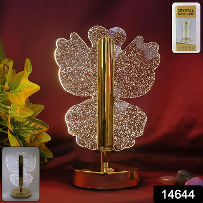 A glowing crystal butterfly lamp with a gold stem and base, against a dark red background with green foliage.