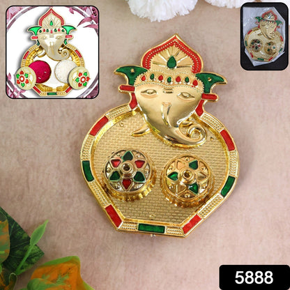 A golden Ganesh pooja thali with two small round containers, accented with red and green enamel details, with a small inset