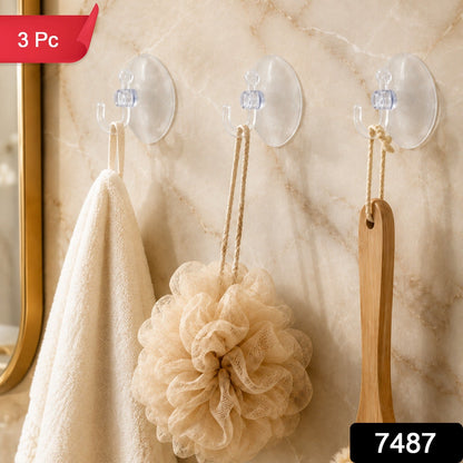 Three transparent suction cup hooks on a marble wall, holding a white towel, a beige loofah, and a wooden brush, with a red