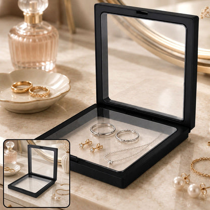 Black square display box with clear film, open to show rings, earrings, and a necklace on a light surface.