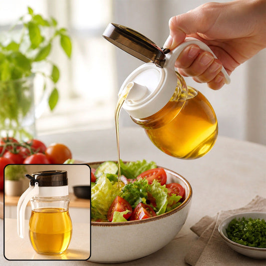 A hand pours oil from a clear dispenser with a white handle and dark lid onto a salad in a bowl, with a smaller dispenser