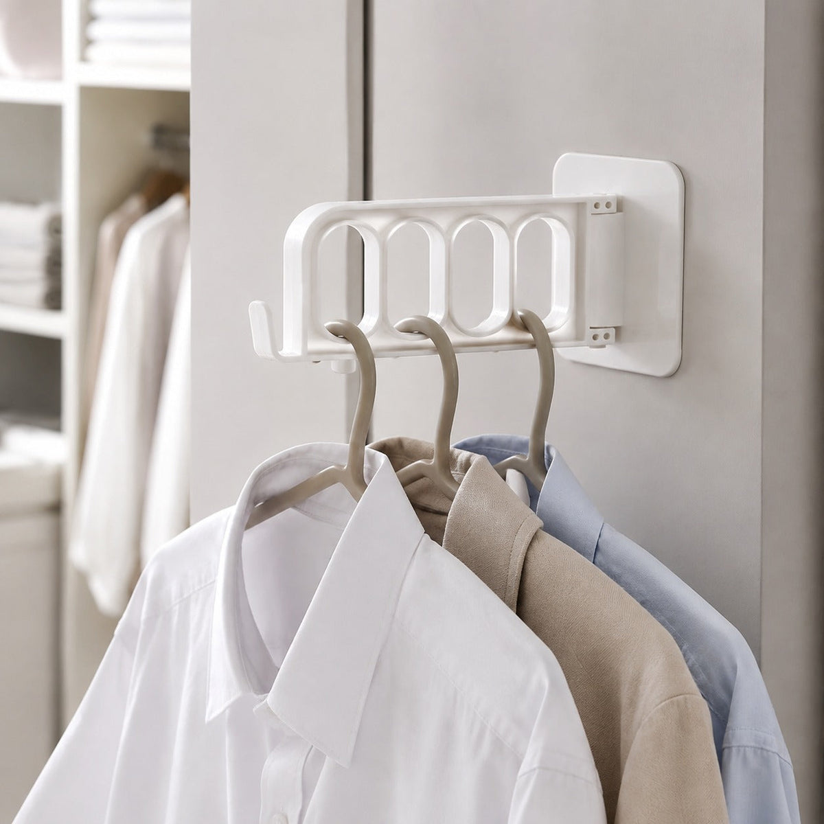 A white foldable wall hook holds three shirts on hangers, with a closet in the soft focus background.