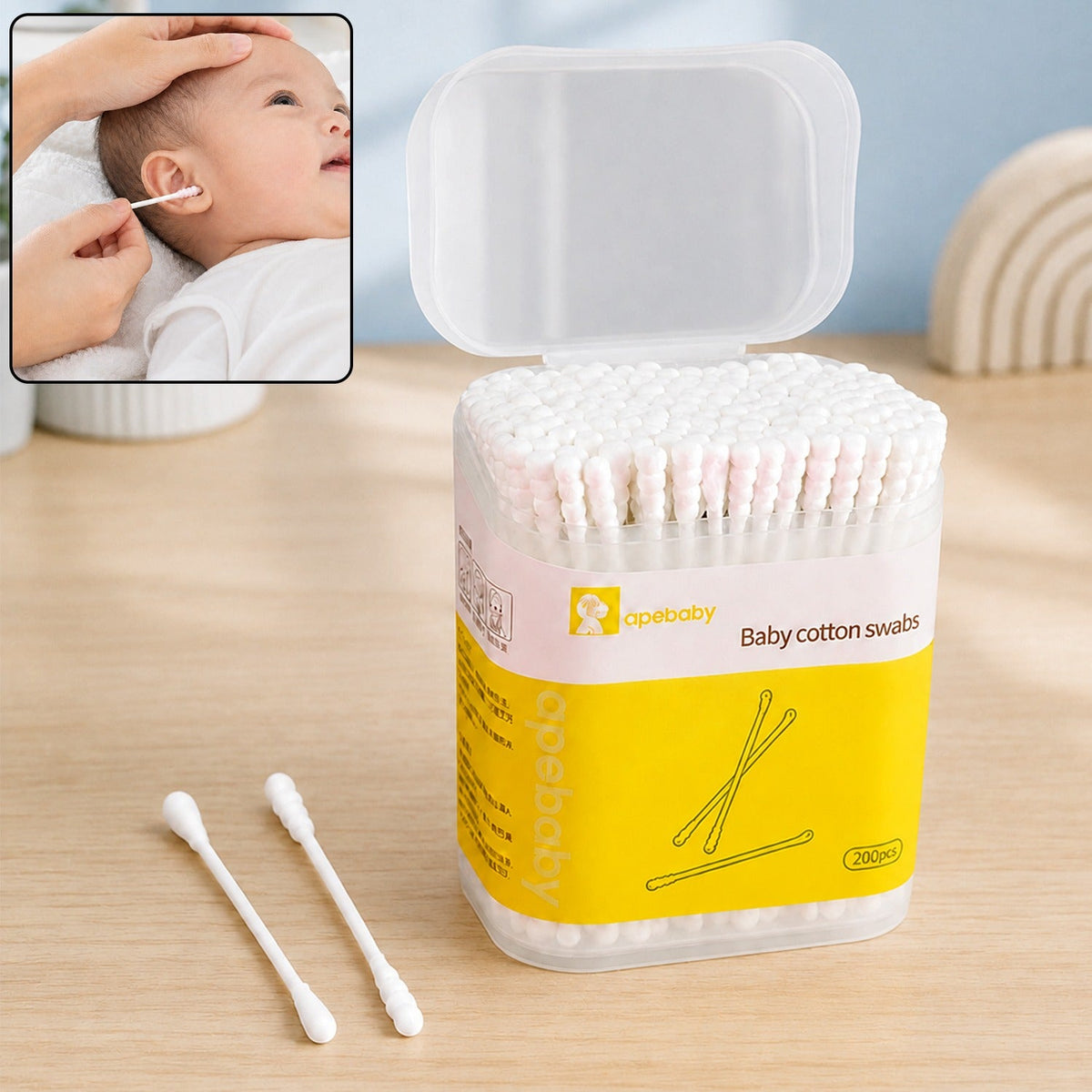 A clear plastic container of white baby cotton swabs with a yellow label, next to two loose swabs, with an inset of a hand