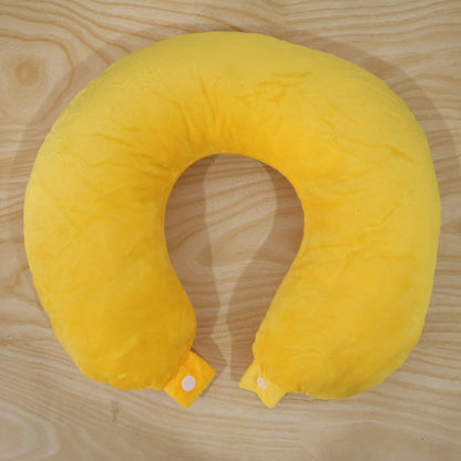 A bright yellow U-shaped neck pillow with two white snap buttons is laid flat on a light brown wooden surface.