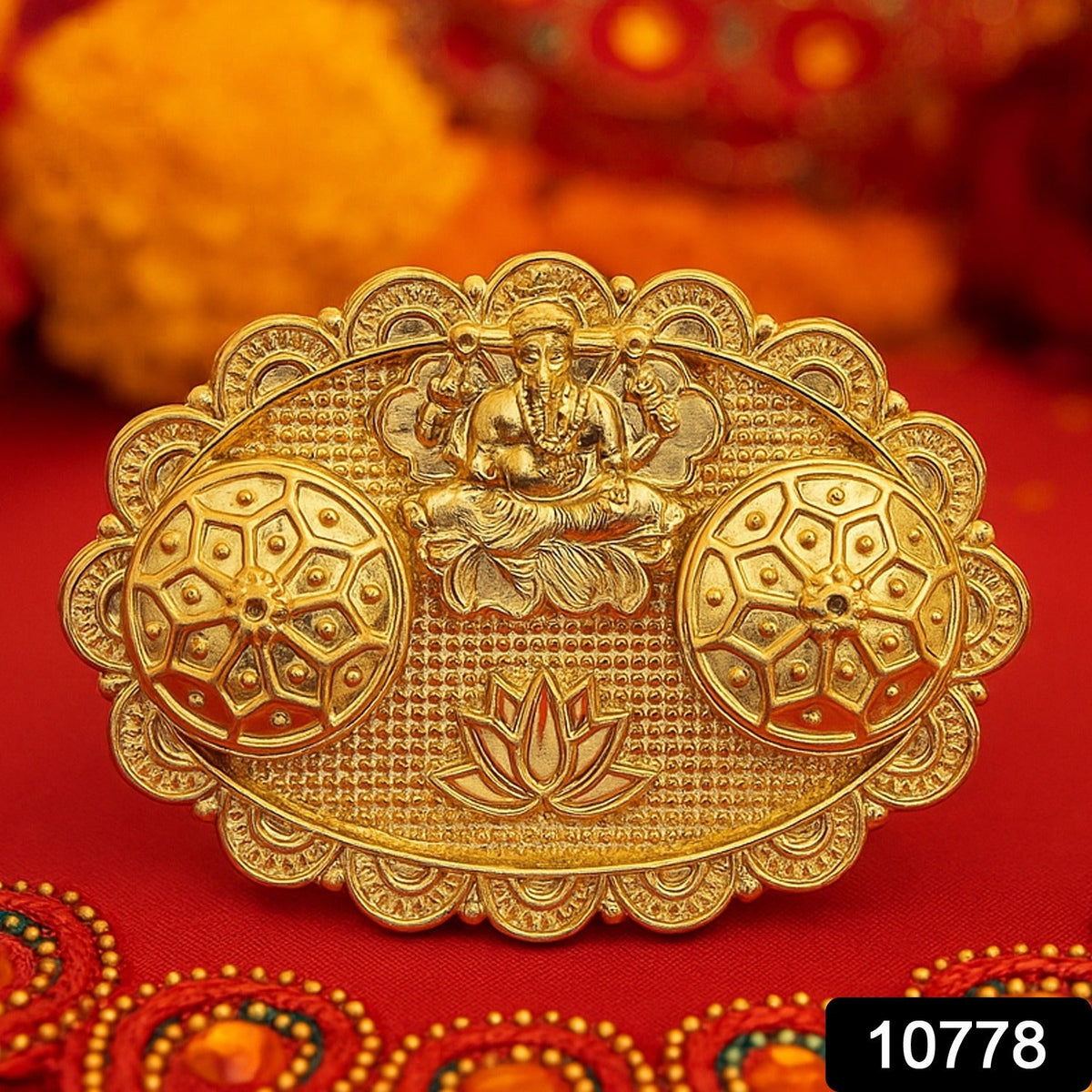 A gold-finished chopra with an embossed Ganesh, two ornate round containers, and a lotus design on a red fabric with