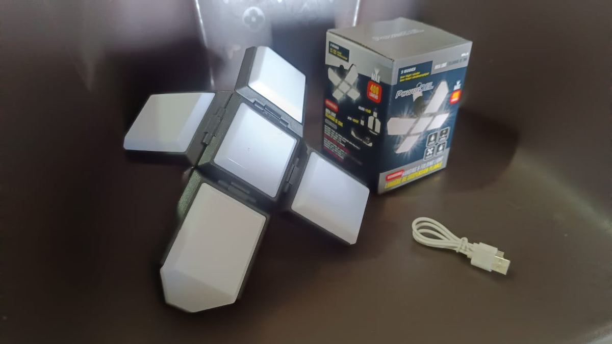 Foldable LED lantern in its expanded form, a white USB charging cable, and its product box on a dark surface.