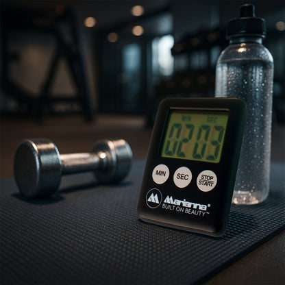 A black digital timer showing 02:03 sits on a black mat next to a dumbbell and a water bottle in a gym setting.