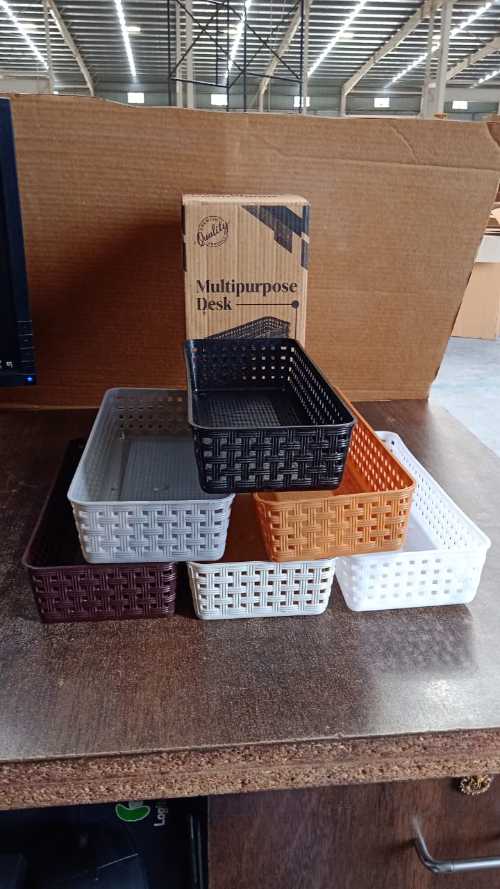 Six rectangular plastic baskets in various colors arranged on a wooden surface with a cardboard box in the background.