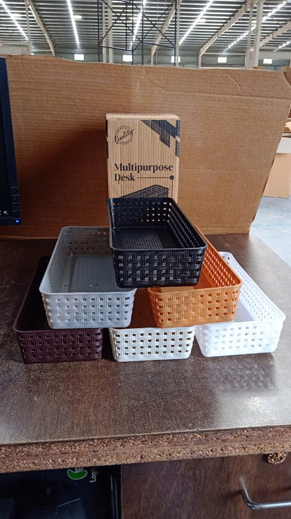Six rectangular plastic baskets in various colors arranged on a wooden surface with a cardboard box in the background.