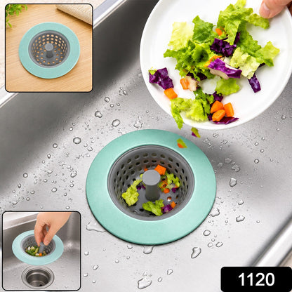 A mint green and gray silicone sink strainer in a stainless steel sink, catching food scraps, with the number 1120 in the