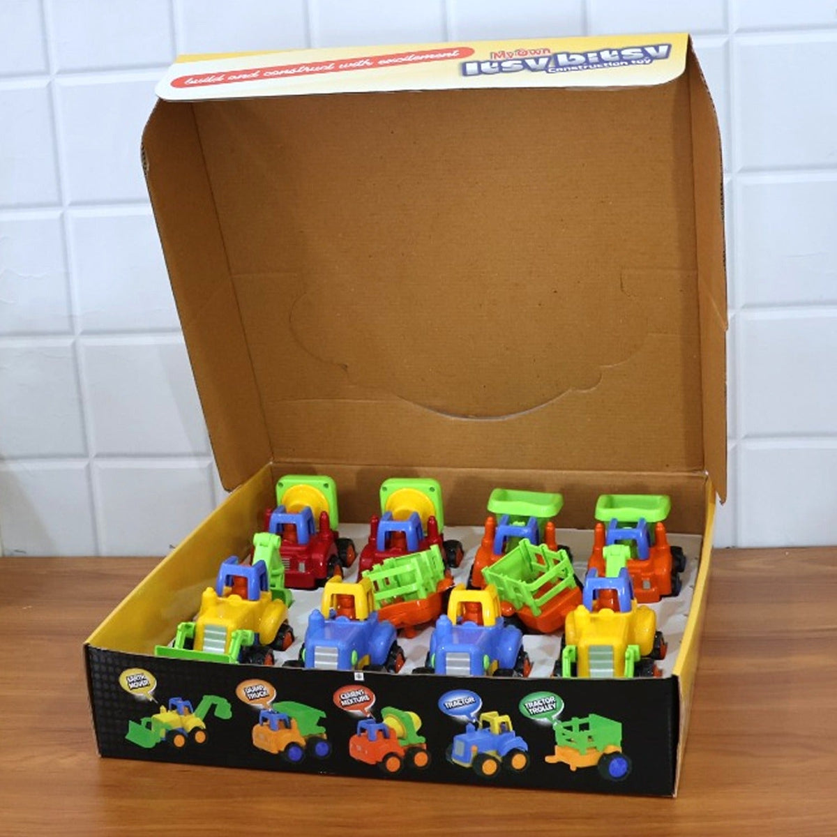 A brown cardboard box filled with eight colorful plastic construction vehicle toys, with the box lid open.