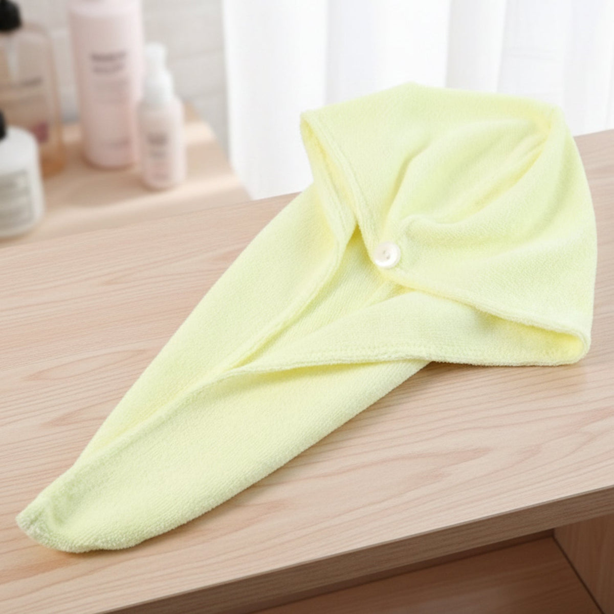A yellow microfiber hair drying wrap towel with a white button is neatly folded on a light brown wooden surface.