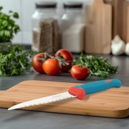 A blue and red paring knife is on a wooden cutting board with fresh tomatoes and herbs in the blurry background.