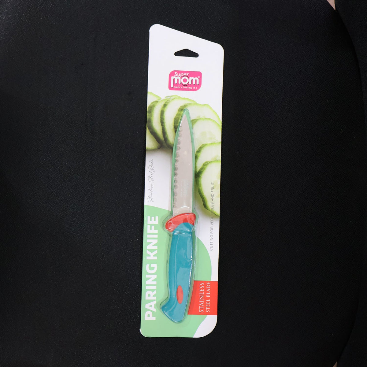 A paring knife with a blue and red handle and serrated blade is sealed in its retail packaging against a dark background.