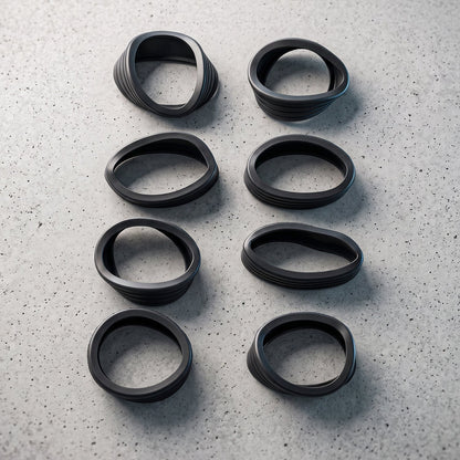 Eight black silicone rings, some slightly distorted, arranged in two vertical rows on a textured grey concrete surface.
