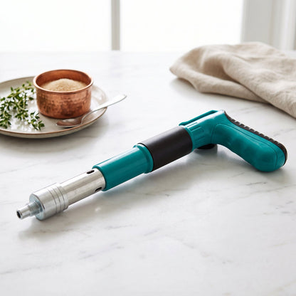 A teal and black manual nail gun rests on a white marble surface next to a small copper bowl and fresh herbs.