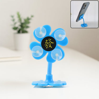 A blue flower-shaped phone holder with suction cups and a Chinese character sits on a white surface.