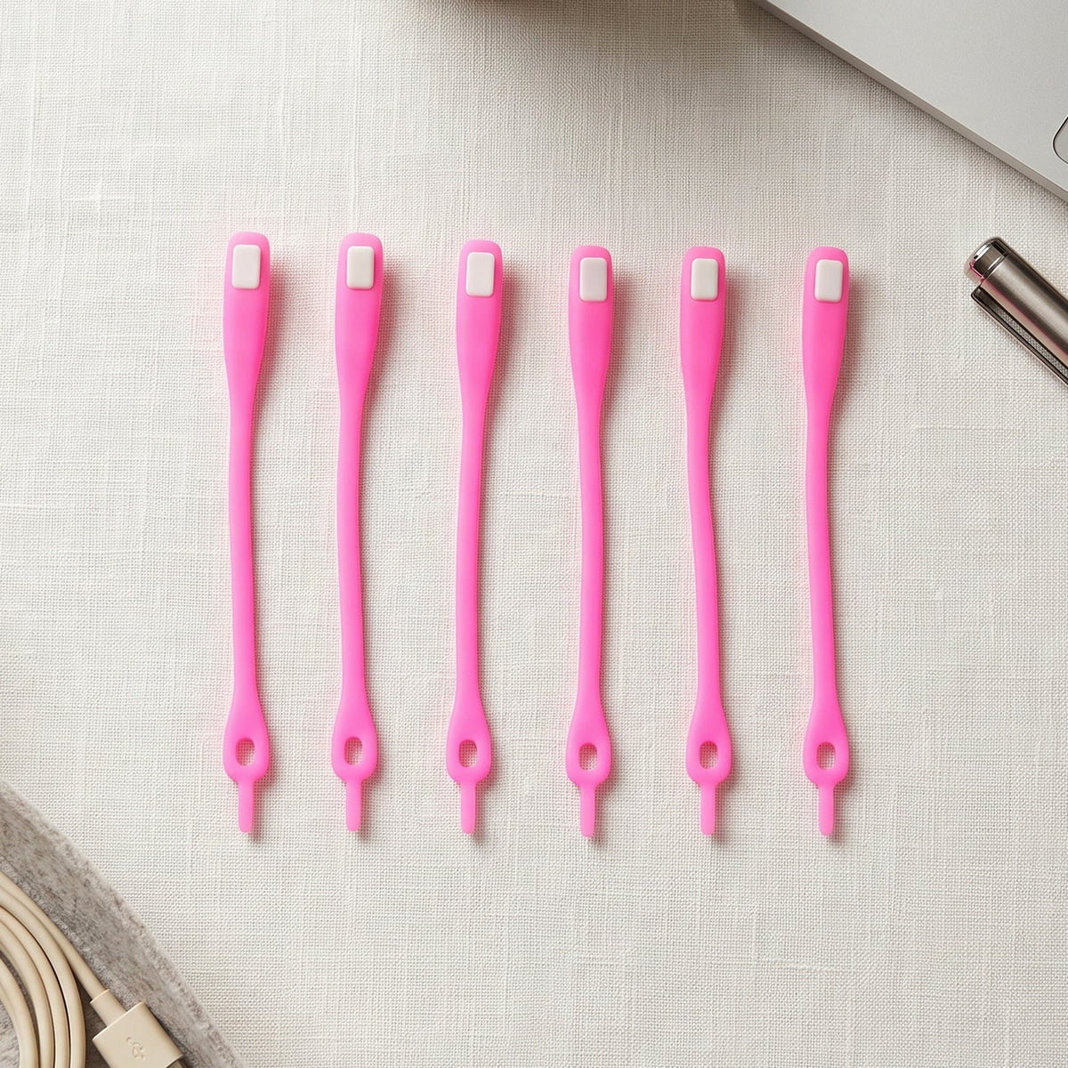 Six bright pink silicone no-tie shoelaces with white clasps, neatly arranged on a white textured surface next to a laptop.