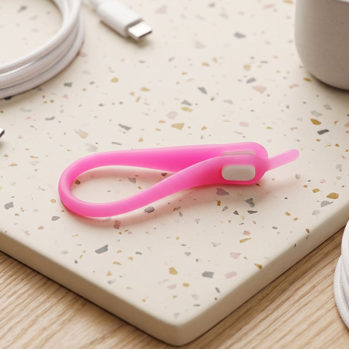 A single pink silicone no-tie shoelace with a white clasp, coiled on a speckled white and grey surface.