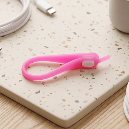 A single pink silicone no-tie shoelace with a white clasp, coiled on a speckled white and grey surface.