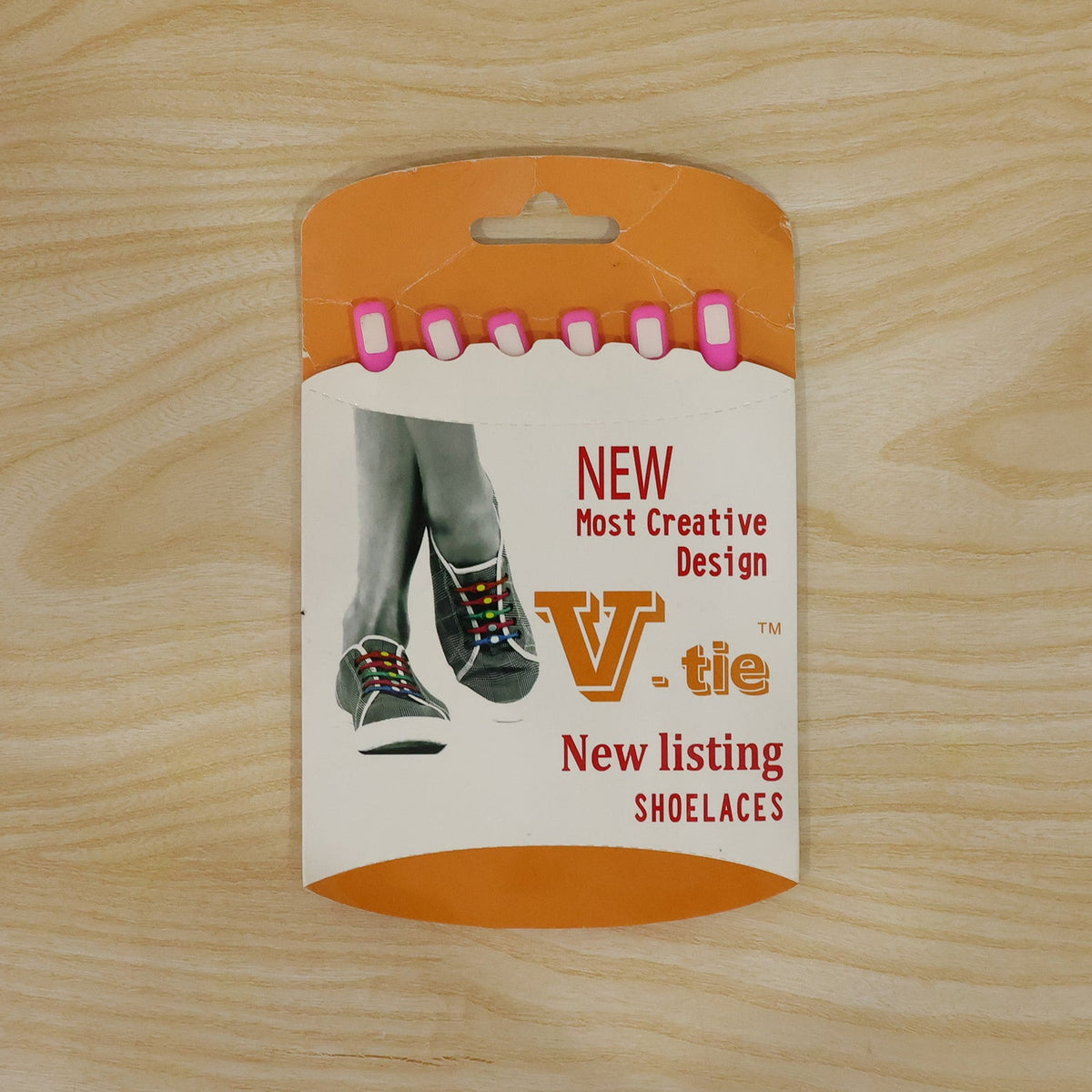 Product packaging for 'V-tie' shoelaces, featuring an orange and white card with text and an illustration of feet in shoes.