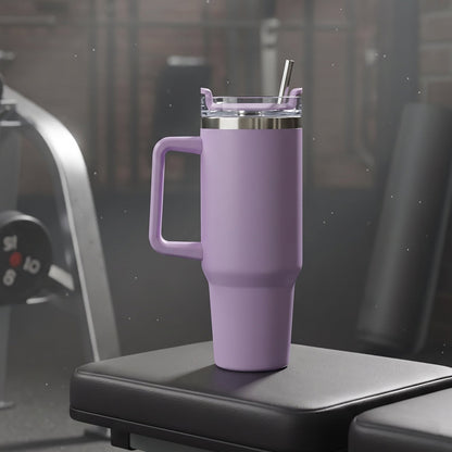 A purple Konvex Hydra Insulated Travel Tumbler with a handle and straw sits on a black gym bench in a dimly lit gym.