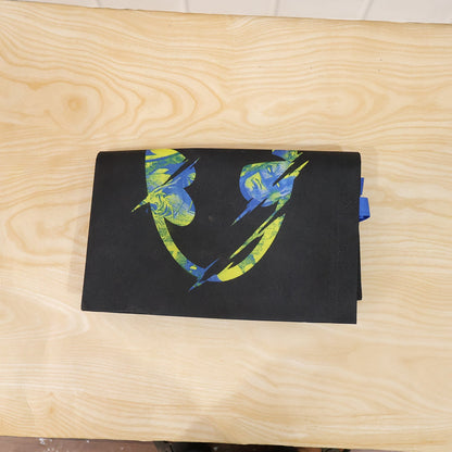 Top-down view of a folded black reusable tote bag with a distressed neon green and blue Batman logo on a light wood surface.