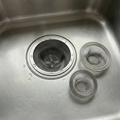 Three stainless steel mesh sink strainers in a stainless steel sink with water droplets.