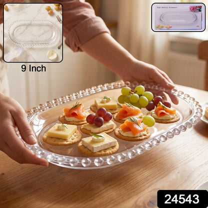A person holds a clear oval glass tray with snacks, showing a 9-inch label and a product code.