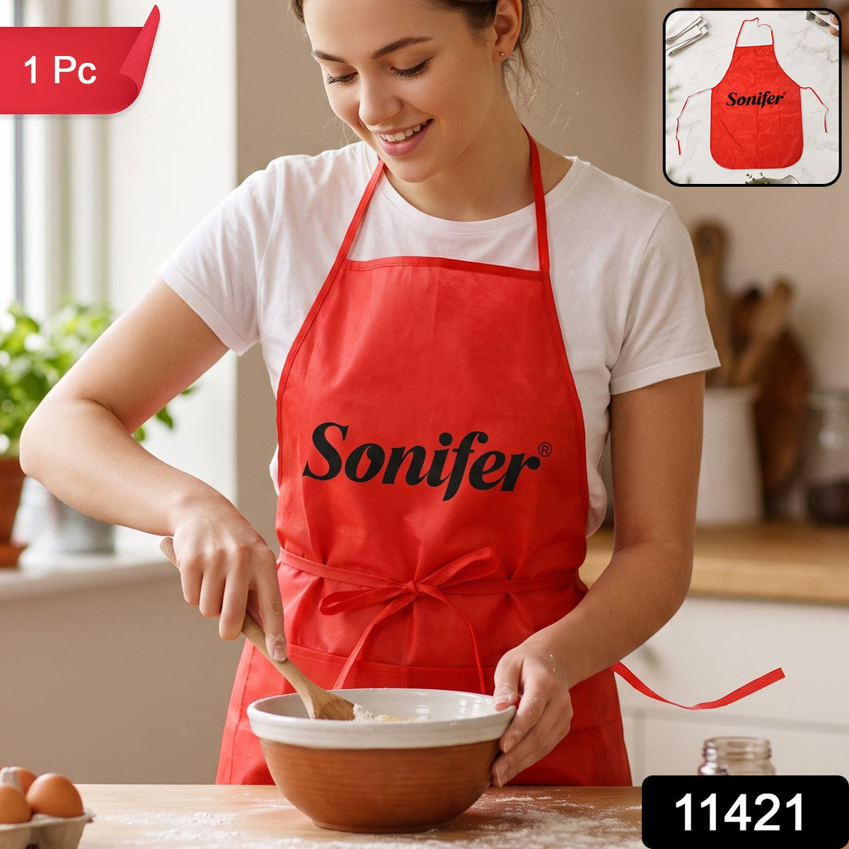 A smiling woman in a white t-shirt and a red Sonifer apron stirs batter in a bowl on a wooden counter, with