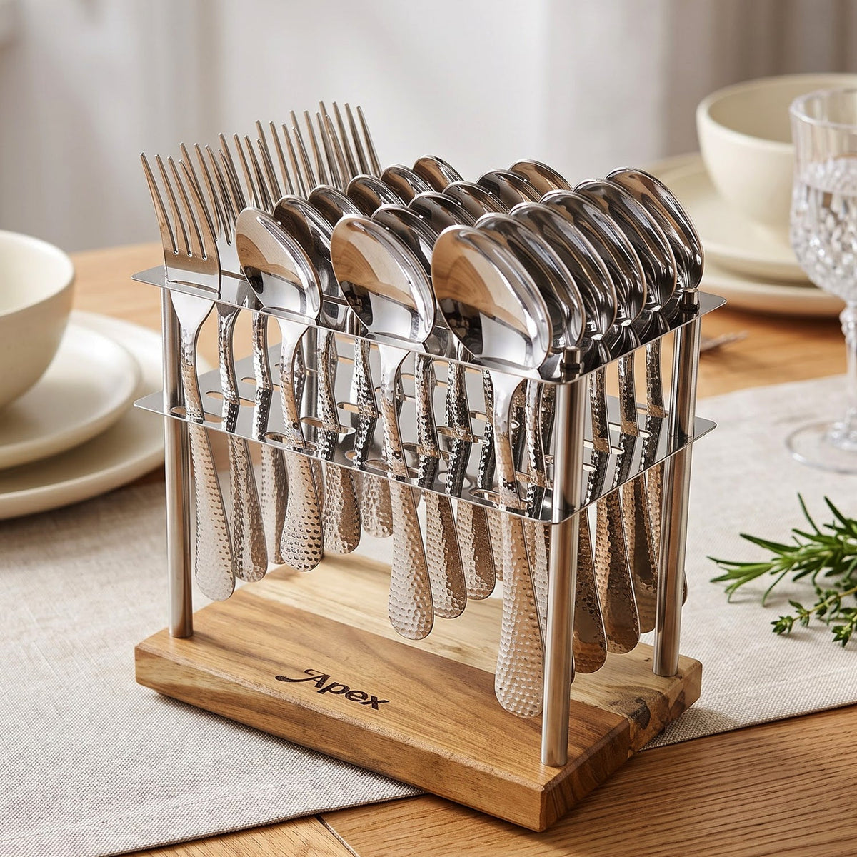 A 24-piece hammered stainless steel cutlery set with a wooden stand on a dining table. The stand has the word "Apex"