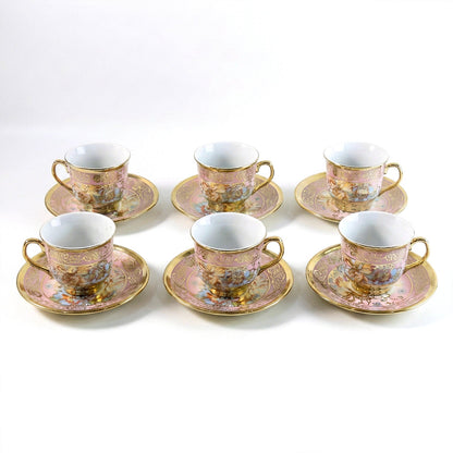 Six pink and gold floral porcelain teacups and saucers with gold rims and handles are neatly arranged on a white surface.