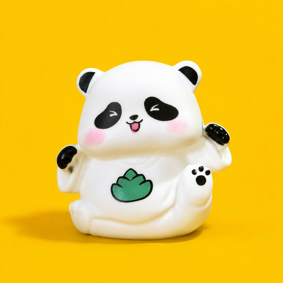 A cheerful white panda night light with black features and a green leaf design on its belly, set against a bright yellow
