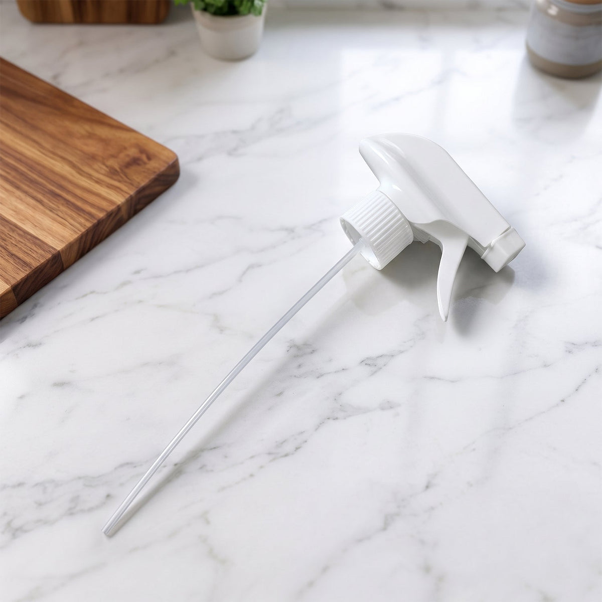 A white plastic spray nozzle with a long tube rests on a white marble countertop next to a wooden cutting board.