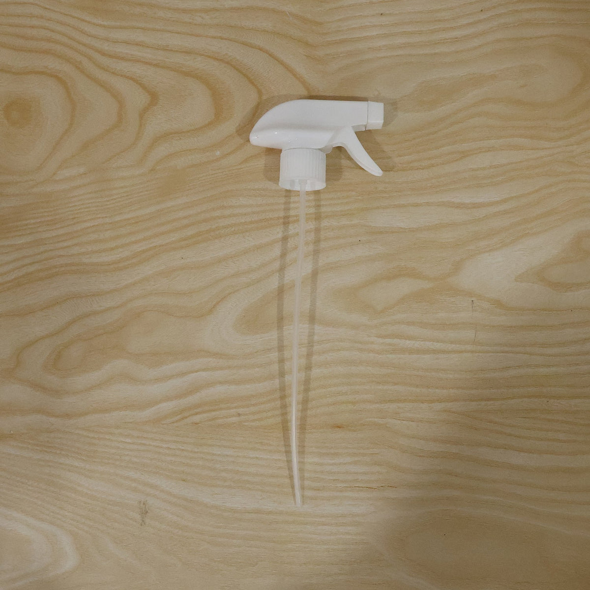 A white plastic spray nozzle with a long, clear tube is centered on a light wooden surface with visible grain.