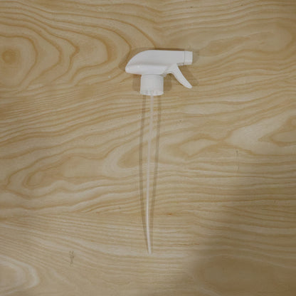 A white plastic spray nozzle with a long, clear tube is centered on a light wooden surface with visible grain.